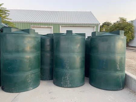 Three vertical, green plastic water tanks with a threaded lid, placed outdoors.